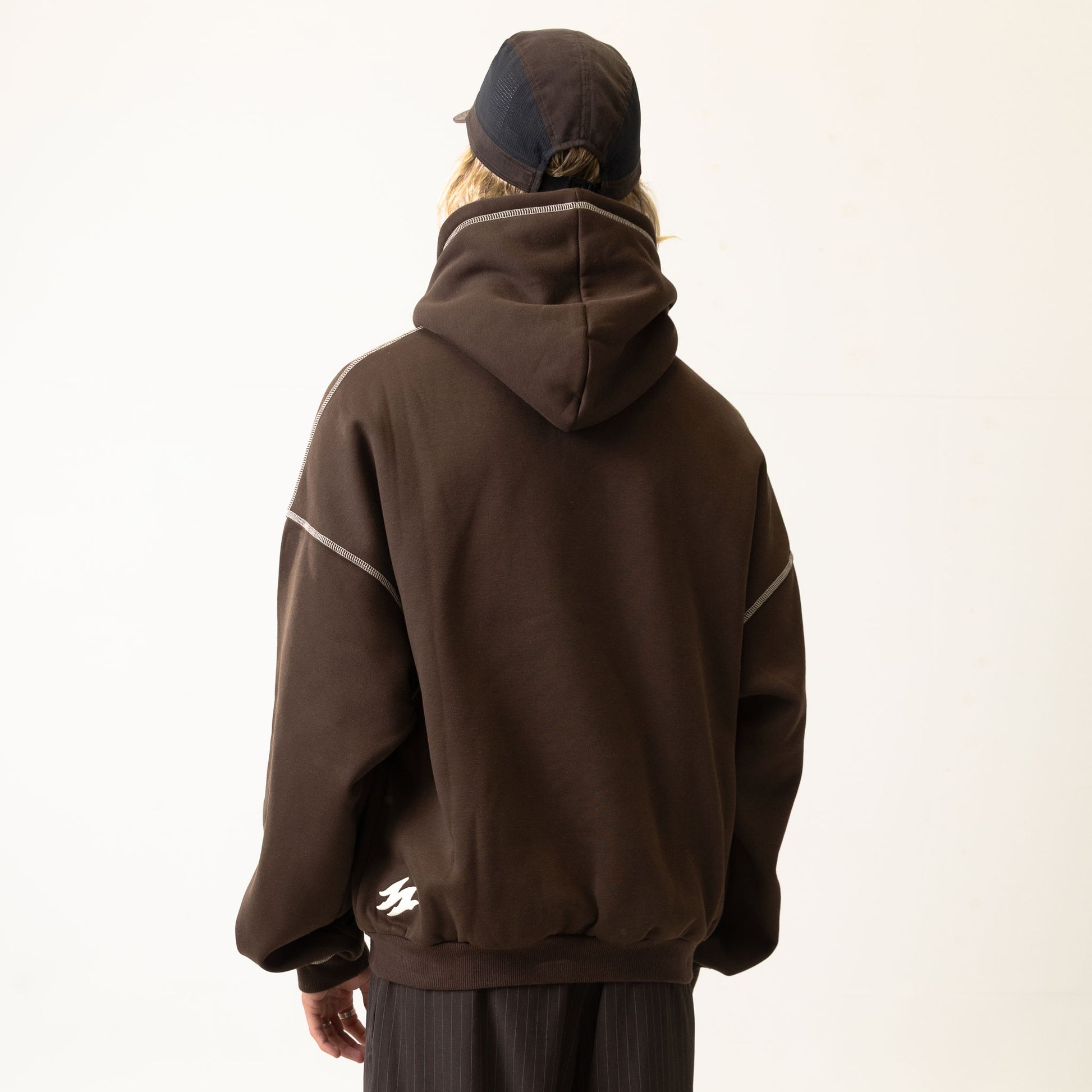 Person wearing a brown hoodie and pants with a cap on a white background