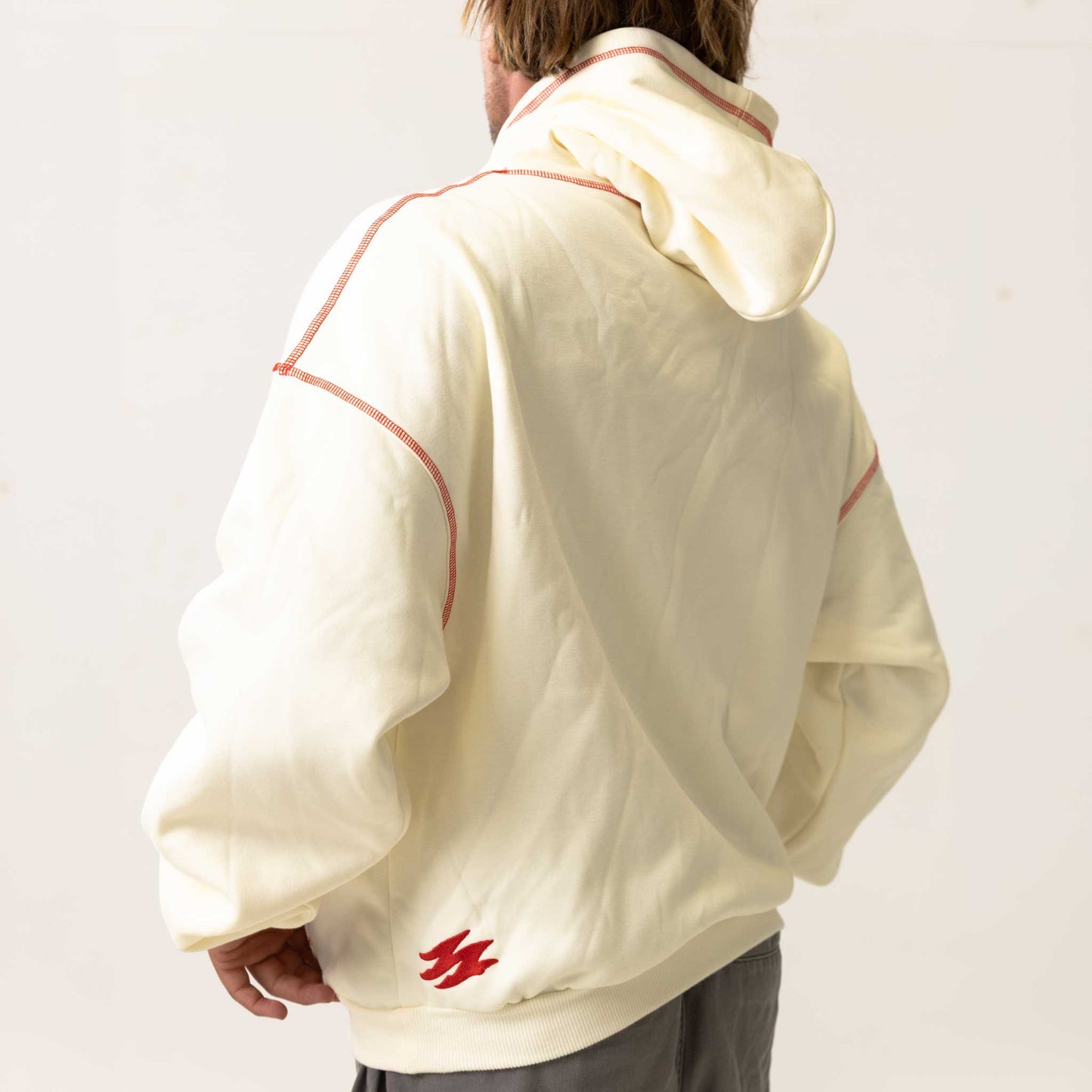 Person wearing a white jacket with red accents and a logo on the back, standing against a plain background.