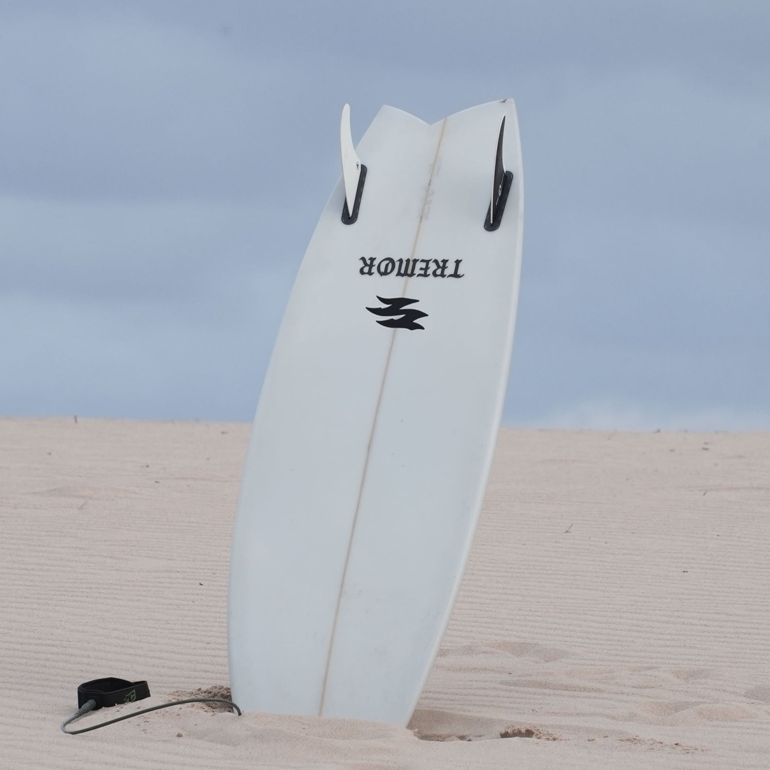 White surfboard with a TREMOR logo on a sandy beach